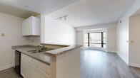 Located at 101 Summer St in the heart of downtown Stamford, Connecticut, this single-floor residence offers a thoughtfully designed layout with a clean, modern aesthetic throughout. The open-concept living and dining area is anchored by wide-plank hardwood-style flooring and a striking angled bay window that frames city views and floods the space with natural light. Track lighting accents the textured ceiling, adding a functional yet stylish touch.

The kitchen is equipped with granite countertops, white cabinetry, and black appliances including a range and built-in microwave. A peninsula counter with an integrated sink provides a natural transition between the kitchen and the living area, making the space ideal for both everyday use and entertaining.

The bedrooms feature plush wall-to-wall carpeting and ample wall space, offering a comfortable and quiet retreat. One bedroom includes an in-unit washer and dryer, adding everyday convenience. The bathroom is finished with classic white tile flooring, a white vanity, and grab bars, reflecting a practical and accessible design.

Throughout the residence, a neutral color palette of whites and soft grays creates a cohesive and inviting atmosphere. The overall layout, as visible in the dollhouse view, is efficient and well-proportioned, making excellent use of the available space in this urban Stamford location.