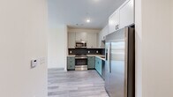 This thoughtfully designed one-bedroom, one-bathroom unit offers a well-utilized single-floor layout with modern finishes throughout. The open-concept kitchen and living area serves as the heart of the space, where the kitchen stands out with two-tone cabinetry—white upper cabinets paired with sage-green lower cabinets—complemented by a dark tile backsplash and a full suite of stainless steel appliances, including a gas range, built-in microwave, dishwasher, and French door refrigerator. Light wood-tone luxury vinyl plank flooring extends throughout the unit, creating a cohesive and clean aesthetic.

The living area benefits from a sliding glass door that opens onto a private balcony with views of surrounding greenery and neighboring architecture, allowing natural light to fill the space. The bedroom is a quiet, self-contained room equipped with a ceiling fan and direct access to a walk-in closet featuring wire shelving for organized storage.

The bathroom is finished with large-format floor tiles, a tub-shower combo with dark mosaic tile surround, a wood-toned vanity with a framed mirror, and matte black fixtures. A dedicated in-unit laundry closet with a stacked washer and dryer adds practical convenience to this efficiently arranged home.
