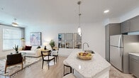 This well-appointed 1-bedroom, 1-bathroom residence offers a smartly organized single-floor layout that maximizes every square foot. A welcoming hallway lined with framed artwork leads into the main living area, setting a clean, contemporary tone from the moment you enter. The open-concept kitchen and living room form the heart of the home, where light wood-style flooring and crisp white walls create a bright, airy atmosphere. The kitchen is equipped with stainless steel appliances, gray shaker-style cabinetry, a subway tile backsplash, and a granite peninsula with bar seating illuminated by pendant lighting — ideal for both cooking and casual dining. The living area benefits from large windows and a glass-paneled door that invite natural light, complemented by a ceiling fan for added comfort. The bedroom is a comfortable retreat featuring a ceiling fan, dedicated closet, and warm accent lighting. The bathroom includes a full soaking tub and shower combination with tile surround and efficient overhead storage. A dedicated closet provides additional storage. Throughout the space, consistent light hardwood flooring, recessed lighting, and neutral tones contribute to a cohesive, modern aesthetic that is both functional and inviting.
