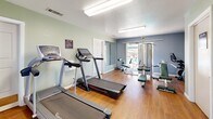 Located at 849 Lincoln Rd in Yuba City, California, this fitness center is a efficiently organized workout facility spread across a single floor. The space is divided into two functional areas designed to support a comprehensive exercise routine.

The main workout room features warm hardwood flooring and is painted in cool, calming tones of sage green and slate blue. It is well-lit by overhead fluorescent fixtures and benefits from natural light streaming through a window that offers a view of an outdoor pool area, creating a bright and motivating atmosphere. This room is equipped with multiple treadmills for cardio training and a multi-station cable machine with adjustable benches for strength and resistance work. A wall-mounted mirror enhances the sense of space and allows users to monitor their form. A posted rules sign reflects the shared-use nature of the facility. Two doors provide easy access to adjacent areas.

The secondary room features rich wood paneling and houses a sauna, offering a dedicated space for post-workout relaxation and recovery. Together, the two rooms deliver a practical and well-appointed fitness environment suited for both cardiovascular and strength training needs, complemented by the added benefit of on-site sauna access.