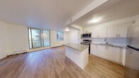 This 2-bedroom, 1-bathroom unit is thoughtfully laid out across a single floor, offering a functional and modern living environment. The open-concept kitchen and living room serves as the heart of the unit, featuring white cabinetry, stainless steel appliances including a range, microwave, and refrigerator, and a central island that provides additional counter and prep space. Hardwood-style flooring flows seamlessly throughout the entire unit, lending a clean, contemporary aesthetic. Large floor-to-ceiling sliding glass doors in the living area fill the space with natural light and provide direct access to an outdoor balcony with exterior views. Baseboard heating runs along the exterior walls, ensuring comfort throughout the seasons. The primary bedroom is a well-sized retreat with its own window offering outdoor views, while the second bedroom is a compact and practical space. Both bedrooms feature the same warm hardwood-style flooring and crisp white walls. A connecting hallway links the private areas of the unit. The bathroom is finished with a full-sized soaking tub and shower combination with white tile surround. The overall design is clean, neutral, and move-in ready.