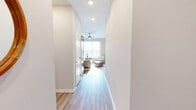 This thoughtfully designed single-floor home offers three bedrooms, two bathrooms, and a functional layout that maximizes every square foot. Light-toned walls and wood-look flooring run throughout, creating a cohesive, airy ambiance brightened by natural light streaming through slatted window blinds.

The open-concept living, dining, and kitchen area forms the heart of the home. The kitchen is a standout feature, equipped with rich dark-stained cabinetry, granite countertops, black appliances, and a large central island with seating — ideal for both cooking and casual dining. Pendant lighting adds a modern touch overhead. The dining area adjoins the kitchen and receives generous natural light.

The primary bedroom offers a comfortable retreat with direct access to an en-suite bathroom featuring a granite-topped vanity with dark cabinetry and a glass-enclosed walk-in shower with tile flooring. A dedicated walk-in closet with wire shelving provides ample storage.

The additional bedrooms are well-proportioned, with one featuring a large window with treetop views. The home also includes a dedicated laundry room, a hallway connecting the private quarters, a welcoming entrance, and four closets distributed throughout for abundant storage. A ceiling fan in the living area enhances comfort year-round.