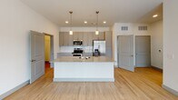Located at 355 Walnut St in Chattanooga, TN, this single-floor unit offers a clean, contemporary design with a bright and open layout. The open-concept kitchen serves as the centerpiece of the living space, showcasing a large island with granite countertops, a built-in sink, and pendant lighting above. Gray shaker-style cabinetry lines the walls, complemented by a white subway tile backsplash and a full suite of stainless steel appliances, including a range, over-the-range microwave, and French door refrigerator. Light hardwood flooring extends throughout the main living areas, creating a warm and cohesive aesthetic. The living area is generously sized, featuring a ceiling fan, large windows that invite natural light, and a glass door providing access to an outdoor space with neighborhood views. The bedroom offers a comfortable, carpeted retreat with a walk-in closet equipped with built-in shelving. The bathroom is finished with clean white subway tile surrounding a soaking tub and shower combo, accented by brushed nickel fixtures. The unit's neutral color palette, modern finishes, and thoughtful layout make it a well-appointed and functional living space in the heart of Chattanooga.