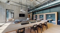 Located at 367 Orange St in New Haven, CT, this single-floor space is a masterclass in industrial-modern design. Expansive floor-to-ceiling windows flood the interior with natural light, offering views of the surrounding streetscape while highlighting the raw, exposed concrete walls and ceilings that define the architectural character throughout.

Light oak hardwood flooring runs the length of the space, providing a warm counterpoint to the industrial palette of concrete, steel, and exposed ductwork overhead. The open-plan layout features distinct zones, including a communal lounge area anchored by plush seating, a cozy fireplace with an artisan shelving display, and pendant lighting with sculptural forms. A bar and café area with open shelving and counter seating serves as a central social hub.

Private nook seating pods with acoustic paneling and warm lighting offer quieter retreats, while wood-framed built-in bench alcoves backed by raw concrete walls provide intimate settings. A repurposed shipping container serves as a bold architectural focal point near the entrance, complemented by a slatted wood ceiling installation and steel elevator bays clad in patinated metal paneling. The space seamlessly blends raw materials with refined furnishings for a dynamic, inviting atmosphere.