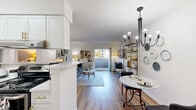 Located at 2134 S Goebbert Rd in Arlington Heights, IL, this 1-bedroom, 1-bathroom residence offers a well-planned, single-floor layout that maximizes every square foot. The open-concept living area seamlessly integrates the kitchen, dining room, and living room into one cohesive space. The kitchen features white cabinetry and a peninsula that doubles as a casual bar or prep area. A stylish chandelier anchors the dining nook, while the living room is bathed in natural light from a sliding glass door that opens directly onto a private patio, extending the living space outdoors. Light wood-toned flooring runs throughout, creating a warm and consistent aesthetic. The bedroom offers a cozy retreat with a two-tone painted accent wall in muted grey and white, a natural light-filled window, and ample closet space — with three closets total throughout the unit. The bathroom is clean and bright, featuring white cabinetry, a large mirror with modern vanity lighting, and wood-look flooring that ties seamlessly into the rest of the home. Overall, the unit presents a bright, modern ambiance with practical, efficient design elements suited for comfortable everyday living.