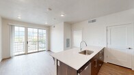 Located at 144 25th St in Ogden, Utah, this single-floor unit offers a thoughtfully designed open-concept layout that maximizes every square foot. The living and kitchen areas flow seamlessly together, anchored by a sleek kitchen island with a white quartz countertop, an undermount sink, and bar-height seating. Dark walnut cabinetry contrasts beautifully with the light countertops, while stainless steel appliances — including a refrigerator, range, microwave, and dishwasher — complete the modern aesthetic. Warm wood-look flooring runs throughout the main living areas, enhancing the bright, contemporary feel of the space. Large sliding glass doors lead to a private balcony, allowing natural light to fill the open living area. The bedroom is a comfortable, carpeted retreat featuring a sliding double-door closet and a gridded window that brings in additional natural light. The full bathroom is finished with the same dark wood cabinetry as the kitchen, a white quartz vanity top, a large wall mirror, and a full tub-shower combination, all set on wood-look flooring that ties the space together cohesively. Clean lines, neutral tones, and modern finishes define the overall ambiance of this well-appointed unit.