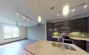Located at Aura 5318 in Grand Prairie, Texas, this single-floor residence offers a thoughtfully designed open-concept layout that seamlessly connects the kitchen, dining, and living areas. The kitchen is a standout, showcasing rich dark cabinetry, a green subway tile backsplash, granite countertops, and a full suite of stainless steel appliances including a refrigerator, electric range, microwave, and dishwasher. A granite-topped island with an undermount stainless steel sink and a gooseneck faucet serves as a central hub, illuminated by stylish pendant lighting. Track lighting runs throughout the main living area, which features warm-toned wood-look flooring and a ceiling fan, creating a bright and inviting atmosphere. Natural light flows in through windows fitted with blinds. The bedroom is generously sized with plush carpet, a ceiling fan, a window, and access to a spacious closet. The bathroom is well-appointed with a granite double vanity, dark cabinetry, wood-look flooring, a full soaking tub with large-format tile surround, and a wide mirror. The overall design blends contemporary finishes with a clean, neutral palette for a modern and comfortable living environment.
