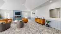 Located at 425 Mill Creek Dr in North Kingstown, Rhode Island, this single-floor community clubhouse offers a well-appointed amenity space designed for both relaxation and active living. The entrance features a welcoming reception area with a front desk accented by a warm yellow counter, a bold blue accent wall, and frosted double glass doors that fill the foyer with natural light and complement the light tile flooring.

The main lounge is a comfortable and thoughtfully designed gathering space, highlighted by a blue shiplap feature wall housing a linear fireplace and wall-mounted television. Vaulted ceilings enhance the sense of openness, while patterned carpeting, blue wainscoting, and warm neutral tones create a cohesive coastal aesthetic. Seating includes a tufted cognac leather sofa, upholstered accent chairs, and a mid-century modern wood credenza with a coffee station. Nautical-themed artwork adds a local character to the walls.

An adjacent multipurpose room provides additional gathering space with a dining table and chairs, supplementary lounge seating, and access to the outdoors through white-shuttered French doors that allow abundant natural light.

The fitness center is generously equipped with cardio machines including treadmills, a stair climber, and a stationary bike, alongside a multi-station strength training unit, free weights, medicine balls, and a rowing machine, all set on durable rubber flooring beneath a distinctive blue-painted ceiling.