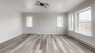 Located on W Madison Street in Chicago, this single-floor unit offers an efficiently designed layout that combines a kitchen and living area, one bathroom, and a closet. The open-plan main space is finished with wood-look luxury vinyl plank flooring in warm gray tones, neutral light gray walls, and white trim, creating a cohesive, modern aesthetic throughout.

The kitchen is outfitted with two-tone cabinetry—white upper cabinets and gray lower cabinets—complemented by a classic white subway tile backsplash and stainless steel appliances, including a full-size refrigerator, electric range, and over-the-range microwave. Flush-mounted black-framed LED light fixtures provide consistent overhead illumination. The living area benefits from multiple windows fitted with white horizontal blinds, allowing ample natural light and street views. A baseboard heating system runs along the perimeter walls.

The bathroom features large-format gray wall tile surrounding a full soaking tub with shower, a gray vanity with a white basin sink, black matte hardware and fixtures, a framed mirror, and a natural light source from a window above the tub. A dedicated closet provides additional storage. The unit's clean, updated finishes make it a functional and well-appointed space.