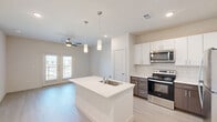 Located at 2700 E Howard Ln in Manor, TX, this thoughtfully designed one-bedroom, one-bathroom unit offers a clean, modern aesthetic throughout. Light wood-style flooring flows seamlessly across the entire space, complementing the bright, neutral palette of the walls and ceilings.

The open-concept kitchen is a standout feature, showcasing a large center island with a white quartz countertop and an undermount sink, illuminated by sleek pendant lighting. Cabinetry combines white upper cabinets with dark lower cabinets, accented by a classic subway tile backsplash. Stainless steel appliances, including a refrigerator, range, and microwave, complete the well-equipped kitchen.

The living area is bright and airy, with a ceiling fan overhead and French doors that open to a private balcony, allowing ample natural light and outdoor views. A secondary window further enhances the natural light in the space.

The bedroom is a comfortable retreat featuring a ceiling fan, a window with neighborhood views, and direct access to a dedicated walk-in closet with built-in shelving and hanging rods.

The bathroom is clean and functional, offering a tiled shower-tub combination, a white quartz vanity countertop, and dark cabinetry consistent with the rest of the unit's design language.
