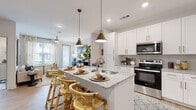 Located in Pooler, Georgia, this single-floor residence offers a well-designed open-concept layout that seamlessly connects the kitchen, dining, and living areas. The kitchen is a standout feature, showcasing crisp white shaker cabinetry with gold hardware, granite countertops, a center island with bar seating, and a full suite of stainless steel appliances including a refrigerator, range, and over-the-range microwave. Pendant lighting with brass-toned fixtures illuminates the island, adding a warm, contemporary touch. Light hardwood-style flooring runs throughout the main living areas, enhancing the bright and airy atmosphere. The living room is generously proportioned, benefiting from large windows that invite natural light and provide outdoor views. A ceiling fan adds comfort, while a private exterior door offers direct access to the outside. The bedroom connects conveniently to a well-appointed bathroom featuring a granite-topped vanity with white cabinetry, a glass-enclosed shower, and direct access to a spacious walk-in closet with built-in shelving and hanging rods. Throughout the residence, a cohesive neutral palette and consistent finishes create a clean, modern aesthetic that is both functional and inviting.