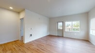 This single-floor unit presents a clean, contemporary design throughout, unified by light hardwood flooring and crisp white walls. The open living area is generously proportioned, offering ample room for flexible furniture arrangements. Natural light enters through multiple windows, including a sliding door that opens to a balcony with outdoor views, enhancing the bright and airy atmosphere.

The kitchen is positioned in an L-shaped configuration adjacent to the living space and is equipped with dark espresso-toned cabinetry contrasted by white countertops and a full suite of white appliances, including a refrigerator, electric range, built-in microwave, and dishwasher. Recessed lighting illuminates the workspace effectively.

A hallway connects the remaining areas of the unit, featuring access to an in-unit laundry closet with a stacked washer and dryer setup. The bathroom includes a dark-cabinetry vanity with a white countertop, undermount sink, and a large frameless mirror. Additional bedrooms are well-sized with natural light provided by individual windows and baseboard heating. The overall design is functional and modern, emphasizing a neutral, cohesive aesthetic throughout.