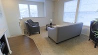 This two-story space offers a thoughtfully designed interior that balances comfort and functionality. The living area serves as a central gathering space, characterized by large windows on multiple walls that flood the room with natural light and provide views of the surrounding neighborhood. The neutral wall tones create a calm, versatile backdrop that complements a range of furnishings and décor styles.

The flooring transitions distinctly between rich hardwood in the entryway or adjoining areas and soft, wall-to-wall carpeting in the main living space, clearly delineating different zones within the open layout. The carpeted living area provides a warm, comfortable feel underfoot, while the hardwood adds a polished, durable contrast near the entry.

The living room is generously proportioned, easily accommodating a sofa, accent chairs, and a central coffee table without feeling crowded. A floor lamp adds ambient lighting to complement the abundant natural light. The overall ambiance of the space is bright, airy, and neutral, making it an inviting environment. The two-story layout further suggests additional living or sleeping spaces above, adding versatility to the overall floor plan.