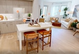 This contemporary 610 square foot apartment in Irvine, CA offers a harmonious blend of style and functionality. The open-concept design maximizes space, seamlessly connecting the living areas. The kitchen is a highlight, boasting sleek light wood cabinetry, stainless steel appliances, and a white quartz island that doubles as a dining area. The living room is bathed in natural light from large windows and features comfortable, modern furnishings. The bedroom, spanning 110 square feet, is a serene retreat with a plush bed, ambient lighting, and sliding glass doors leading to a private balcony. The bathroom impresses with a spacious glass-enclosed shower and built-in storage. Throughout the apartment, warm wood floors, recessed lighting, and a neutral color palette create a cohesive, inviting atmosphere. Smart storage solutions and thoughtful design elements make this compact space feel expansive and luxurious.