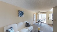 Located at 6304 Rancho Mission Road, unit #166 at The EsSex in San Diego presents a comfortable single-floor residence with a welcoming open-concept design. The living and dining areas flow seamlessly together, creating a cohesive and functional layout suited for everyday living and entertaining.

The living area features neutral-toned carpeting and warm beige walls that lend a calm, inviting atmosphere. A textured ceiling adds subtle architectural character throughout the space. Décor accents, such as a floral canvas print in navy and white, complement the light, airy feel of the interior.

The dining area is positioned adjacent to a large sliding glass door, which serves as a prominent feature of the space. This expansive window allows an abundance of natural light to fill the room while offering views of the surrounding outdoor scenery, including lush greenery visible from the balcony or patio. A ceiling fan with a light fixture is installed nearby, providing both ventilation and ambient lighting.

Overall, the space maintains a relaxed, neutral aesthetic, with consistent flooring and finishes that unify the open living and dining zones. The single-floor layout ensures easy accessibility and a straightforward, functional flow throughout.
