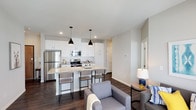 This well-designed single-floor residence offers a thoughtfully planned layout with modern finishes and a cohesive aesthetic throughout. The open-concept kitchen and living area serves as the heart of the unit, where a large granite-topped island with an integrated sink and seating anchors the space. The kitchen is equipped with stainless steel appliances, including a refrigerator, range, and microwave, and features crisp white shaker-style cabinetry extending to the ceiling for ample storage. Stylish black pendant lights hang above the island, complementing the dark hardwood-style flooring that runs throughout the unit. The living area is bright and welcoming, with large windows allowing natural light to fill the room. Each bedroom is comfortably proportioned, featuring windows with views to the exterior, dark hardwood-style floors, and neutral wall tones. The primary bedroom includes a walk-in closet with built-in shelving. The bathrooms are cleanly finished with white cabinetry, granite countertops, full tub-shower combinations, and practical over-toilet storage. The overall ambiance is modern and functional, with a neutral color palette and quality materials creating a polished, move-in-ready environment.