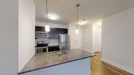 Located at 527 Old Bridge Turnpike in East Brunswick, NJ, this well-appointed 2-bedroom, 2-bathroom residence offers a thoughtfully designed single-floor layout with modern finishes throughout. The open-concept kitchen and living area serves as the heart of the home, anchored by a large granite-topped island with a built-in sink and pendant lighting overhead. Dark espresso cabinetry, stainless steel appliances — including a refrigerator, range, and microwave — and hardwood-style flooring complete the kitchen's polished look. The spacious living area extends naturally from the kitchen, bathed in natural light from large windows and offering access to a private balcony through a glass-paneled door. The generously sized primary bedroom features plush carpeting and connects to a private en-suite bathroom equipped with a glass-door walk-in shower lined with classic white subway tile and a granite vanity. The second bedroom also offers ample space with soft carpeting and easy access to the second full bathroom, which includes a subway-tiled soaking tub and shower combination. Clean white walls, consistent trim work, and a neutral palette create a bright, cohesive ambiance throughout the entire residence.