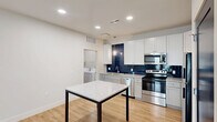 This well-designed one-bedroom, one-bathroom unit in Perrysburg, Ohio offers a thoughtfully laid-out single-floor plan with modern finishes throughout. The open-concept kitchen, dining, and living area serves as the heart of the home, featuring light wood-style flooring, recessed lighting, and a cohesive, contemporary aesthetic. The kitchen is a standout, equipped with white shaker cabinetry, granite-look countertops, a bold navy subway tile backsplash, stainless steel appliances including a range, microwave, dishwasher, and refrigerator, and a central dining table with a granite top. The living area benefits from natural light streaming through glass French doors with transom windows, providing outdoor views and a bright, airy feel. The bedroom offers a comfortable and quiet retreat, finished with plush carpeting, dual windows with exterior views, and two closets — including a walk-in — accessed through distinctive navy interior doors. The full bathroom features a sliding glass-door shower enclosure and wood-style flooring. A dedicated laundry room with a washer and utility storage adds everyday convenience. The unit combines functional design with attractive modern details throughout.