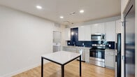This well-designed one-bedroom, one-bathroom unit in Perrysburg, Ohio offers a thoughtfully laid-out single-floor plan with modern finishes throughout. The open-concept kitchen, dining, and living area serves as the heart of the home, featuring light wood-style flooring, recessed lighting, and a cohesive, contemporary aesthetic. The kitchen is a standout, equipped with white shaker cabinetry, granite-look countertops, a bold navy subway tile backsplash, stainless steel appliances including a range, microwave, dishwasher, and refrigerator, and a central dining table with a granite top. The living area benefits from natural light streaming through glass French doors with transom windows, providing outdoor views and a bright, airy feel. The bedroom offers a comfortable and quiet retreat, finished with plush carpeting, dual windows with exterior views, and two closets — including a walk-in — accessed through distinctive navy interior doors. The full bathroom features a sliding glass-door shower enclosure and wood-style flooring. A dedicated laundry room with a washer and utility storage adds everyday convenience. The unit combines functional design with attractive modern details throughout.