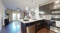 This single-floor residence showcases a thoughtfully designed open-concept layout that seamlessly connects the kitchen, dining, and living areas. The kitchen is a standout feature, equipped with rich dark espresso cabinetry, white quartz countertops, a tile backsplash, and a full suite of stainless steel appliances including a refrigerator, range, microwave, and dishwasher. A peninsula with seating for multiple bar stools provides an ideal casual dining space, while pendant lighting overhead adds a polished finishing touch. Rich hardwood-style flooring runs throughout the main living areas, lending warmth and continuity to the space.

The living room is anchored by a bold burnt-orange accent wall, ceiling fan, and French doors that flood the room with natural light. The bedroom offers plush carpeting, a ceiling fan, and a generously sized window with outdoor views. Adjacent to the bedroom is a well-appointed bathroom featuring dark cabinetry, white countertops, and a tub-shower combination, with direct access to a walk-in closet equipped with built-in shelving and hanging rods. Throughout the residence, consistent design elements and modern finishes create a cohesive and contemporary ambiance.
