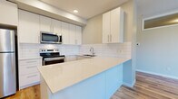 This well-designed 2-bedroom, 2-bathroom unit is situated within a contemporary multi-story building and offers a thoughtfully efficient layout across a single floor. Light hardwood flooring flows consistently throughout the space, contributing to a clean, cohesive aesthetic.

The open-concept kitchen and living area serves as the heart of the unit. The kitchen features crisp white cabinetry extending to the ceiling, stainless steel appliances including a refrigerator, electric range, and built-in microwave, complemented by a white subway tile backsplash and light quartz countertops. A peninsula provides additional prep space and casual seating, opening seamlessly to the living area, which benefits from recessed lighting and a tray ceiling detail.

Both bedrooms are comfortably sized, each featuring large windows that invite natural light and offer views of the surrounding neighborhood. The primary bedroom includes an ensuite bathroom equipped with a single-sink vanity, white cabinetry, and a shower-tub combination. A second bathroom mirrors this clean, functional design. A private balcony accessible from the unit provides outdoor space with views of the building's modern exterior and landscaped surroundings.