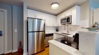 Located at 1801–1803 E 12th St in Cleveland, Ohio, this single-floor unit offers a thoughtfully designed layout with contemporary finishes throughout. The kitchen is a standout feature, outfitted with white shaker-style cabinetry, white subway tile backsplash, quartz countertops, and a full suite of stainless steel appliances including a refrigerator, electric range, microwave, and dishwasher. A peninsula provides additional prep space and casual seating opportunity, while warm hardwood flooring ties the space together.

The unit includes two sleeping areas. One bedroom features soft neutral walls, hardwood floors, a double closet with paneled doors, and understated décor. The second sleeping space is distinguished by a dramatic wall of large windows with horizontal blinds, flooding the room with natural light and offering views of the surrounding urban streetscape.

The bathroom is finished with a marble-look quartz vanity, matte black fixtures, a classic black-and-white basketweave tile floor, white subway tile surround, and a round black-framed mirror, lending a refined yet timeless aesthetic. The 3D floorplan reveals a compact, efficiently organized layout that maximizes the available space. Overall, the unit presents a clean, modern atmosphere well-suited to urban living in Cleveland.
