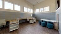 Located at 1901–1931 Hanahan Rd in North Charleston, South Carolina, this single-floor office space offers a clean, contemporary work environment designed with both functionality and style in mind. The interior is defined by a striking two-tone shiplap wall treatment — crisp white on the upper half and a soft slate blue below — that runs throughout, lending the space a modern yet inviting character.

Elevated ceilings amplify the sense of openness, while a generous band of clerestory windows along the upper walls floods the interior with natural light throughout the day. The wood-look plank flooring grounds the space with a warm, professional aesthetic that complements the light furnishings.

The workspace is configured to support collaborative and individual work alike. Multiple workstation clusters with wood-top desks and built-in storage provide ample room for focused tasks, while a casual seating area featuring a white table and teal upholstered ottomans encourages informal meetings and collaboration. A wall-mounted display screen further supports presentations or team gatherings. Additional storage cabinetry with a natural wood finish is thoughtfully integrated along the walls.

Black-framed glass doors with frosted panels define the entry points, adding a sleek, contemporary touch. Overall, the space strikes a balance between a polished professional environment and a welcoming, well-lit atmosphere well-suited for a productive workday.