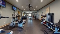 This fitness facility in Columbus, Georgia is a comprehensively outfitted exercise space designed to support a wide range of workout routines. The single-level layout provides generous open floor space covered in durable rubber flooring, ideal for both equipment use and free movement. Soft blue-gray walls are complemented by warm wood trim along the crown molding and door frames, creating a polished yet functional environment.

The cardio section features multiple treadmills and elliptical trainers from True Fitness, as well as a stationary bike and rowing machine, all positioned for easy access. Wall-mounted flat-screen televisions are positioned throughout the room for entertainment during workouts. The strength training area includes a multi-functional cable and power rack system, a dumbbell rack with a full range of weights, and an adjustable bench.

Full-length mirrors line one wall, visually expanding the space and allowing users to monitor their form. A medicine ball rack and stability balls add functional fitness options. French doors along one wall invite natural light and provide outdoor access. Recessed lighting and dual ceiling fans ensure the space remains well-lit and comfortable. A hallway connects to an additional room, adding utility to the overall facility.