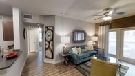 Located at 135 Old San Antonio Rd in the charming Hill Country town of Boerne, Texas, this single-story residence offers a thoughtfully designed open-concept layout that seamlessly connects its key living areas. The living room serves as the heart of the home, featuring warm wood-look flooring, neutral-toned walls, and a ceiling fan that enhances the comfortable atmosphere. Stylish décor accents — including a striking oversized geode-inspired wall art piece and an ornate mirror — add character and visual interest to the space. A teal sofa and coordinating accent chairs create an inviting seating arrangement, complemented by layered lighting from table lamps and recessed fixtures. The open floor plan flows naturally into the kitchen and dining areas, where dark cabinetry and a central island provide both functionality and elegance. The dining space accommodates comfortable gatherings, while the kitchen is well-equipped for everyday use. Throughout the home, consistent wood-look flooring ties the spaces together, creating a cohesive and modern aesthetic. Ceiling fans are present in multiple rooms, ensuring year-round comfort. The overall ambiance is warm, contemporary, and welcoming — ideal for both relaxing and entertaining in the heart of the Texas Hill Country.