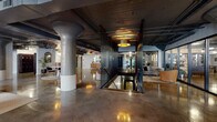 This impressive single-floor space masterfully blends industrial heritage with contemporary design across a generous footprint. Polished concrete floors reflect warm pendant lighting throughout, creating a dynamic interplay of light and texture. Structural concrete columns rise prominently, anchoring the open layout while preserving the raw, warehouse-era character of the building. Exposed ceilings reveal original wood planking, painted dark, alongside visible ductwork and conduit that add to the space's authentic industrial aesthetic.

The floor plan flows through several distinct zones, each purposefully furnished. A welcoming lounge area features tufted sofas, leather armchairs, and vintage-style rugs, while a separate dining and collaborative zone offers long communal tables surrounded by mixed seating. Arched doorways and black steel slat partitions provide subtle spatial definition without sacrificing the openness of the layout. Full-height steel-framed windows along exterior walls flood the space with natural light and offer views outward.

Additional areas include a glass-partitioned private lounge, a casual dining nook with built-in bench seating and wall-mounted artwork, and a dedicated laundry room equipped with extensive white cabinetry, a continuous countertop, and polished concrete floors. The overall ambiance is sophisticated yet inviting, balancing rugged architectural bones with refined, curated furnishings.