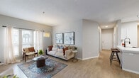 Located at 10 Gentrys Walk in Atlanta, Georgia, this single-floor residence offers a well-designed layout with an open-concept living, dining, and kitchen area that promotes a seamless flow throughout the space. The living room is anchored by light hardwood-style flooring, a textured ceiling, and a decorative fireplace framed in tile, with large windows and a sliding glass door that invite abundant natural light and outdoor views. A dedicated dining area sits adjacent to the kitchen, which features a galley-style design with white upper cabinetry, contrasting gray lower cabinets, quartz countertops, a deep sink with a matte black faucet, and a full suite of stainless steel appliances including a gas range, microwave, dishwasher, and refrigerator. A breakfast bar with counter seating provides additional dining flexibility. The hallway connects the living areas to the bedrooms, each of which showcases a distinctive tray ceiling that adds architectural character. The primary bedroom is generously proportioned and benefits from natural light through large windows with blinds. The bathroom includes a walk-in shower with sliding glass doors and clean white finishes. Throughout the space, neutral gray walls and consistent hardwood-style flooring create a cohesive, modern aesthetic.