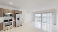 This modern 2-bedroom, 2-bathroom unit at 25850 SW 140th Ct, Homestead, FL offers a clean, contemporary design across a single floor. Polished large-format white tile flooring runs throughout, reflecting natural light and creating a bright, cohesive feel. The open-concept kitchen and living area serve as the heart of the unit, where the kitchen features warm wood-toned cabinetry extending to the ceiling, a full suite of stainless steel appliances including a French door refrigerator, electric range, built-in microwave, and dishwasher, all complemented by a crisp white countertop and recessed lighting. The spacious living area opens to natural light through vertical-blind-covered sliding doors. Both bedrooms are well-proportioned, bright, and serviced by individual wall-mounted mini-split air conditioning units for personalized climate control. The primary bedroom includes a dedicated closet. Each bathroom is finished with striking marble-patterned tile surrounds in the walk-in showers, floating vanities with undermount sinks, and modern chrome fixtures. One bathroom features a darker vanity, while the other offers a wood-toned finish, adding subtle variety. A hallway connects the living spaces efficiently, completing this clean and functional layout.