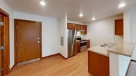 This single-floor unit offers a clean, functional layout designed for comfortable everyday living. The kitchen is equipped with stainless steel appliances—including a refrigerator and range—complemented by warm wood-toned cabinetry, light countertops, a sink peninsula, and recessed lighting overhead. Light hardwood-style flooring runs through the kitchen and entry area, adding a welcoming warmth to the space.

The two bedrooms are generously sized, each featuring plush wall-to-wall carpeting, rich wood baseboards, and windows that allow natural light to filter in. The primary bedroom includes direct access to a walk-in closet with built-in shelving, as well as an en-suite bathroom. Both bathrooms are finished with tile flooring, wood-cabinet vanities, white countertops, large mirrors, and tub/shower combinations.

A dedicated laundry area houses a full-size Amana washer and dryer side by side, with a wire shelf mounted above for added storage convenience. Throughout the unit, neutral white walls, consistent warm wood trim, and ceiling-mounted light fixtures create a cohesive and tidy aesthetic. The overall layout is practical and efficient, making excellent use of the available space across each room.