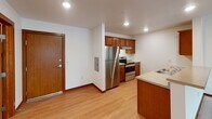 This single-floor unit offers a clean, functional layout designed for comfortable everyday living. The kitchen is equipped with stainless steel appliances—including a refrigerator and range—complemented by warm wood-toned cabinetry, light countertops, a sink peninsula, and recessed lighting overhead. Light hardwood-style flooring runs through the kitchen and entry area, adding a welcoming warmth to the space.

The two bedrooms are generously sized, each featuring plush wall-to-wall carpeting, rich wood baseboards, and windows that allow natural light to filter in. The primary bedroom includes direct access to a walk-in closet with built-in shelving, as well as an en-suite bathroom. Both bathrooms are finished with tile flooring, wood-cabinet vanities, white countertops, large mirrors, and tub/shower combinations.

A dedicated laundry area houses a full-size Amana washer and dryer side by side, with a wire shelf mounted above for added storage convenience. Throughout the unit, neutral white walls, consistent warm wood trim, and ceiling-mounted light fixtures create a cohesive and tidy aesthetic. The overall layout is practical and efficient, making excellent use of the available space across each room.