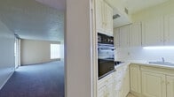 This single-floor, 2-bedroom, 1-bathroom unit offers a practical and well-organized layout designed to maximize its comfortable footprint. The living area features soft wall-to-wall carpeting, neutral-toned walls, and a textured ceiling, creating a warm and inviting atmosphere. A pass-through window connects the living space directly to the kitchen, enhancing the open feel between the two areas. Sliding glass doors lead out to a balcony, allowing natural light to fill the room and providing outdoor access with open views.

The kitchen is equipped with white cabinetry featuring gold-tone hardware, a built-in wall oven, a cooktop, and a stainless steel refrigerator. Light tile flooring runs through the kitchen and hallway areas, providing a clean contrast to the carpeted rooms.

The spacious primary bedroom is generously sized, featuring large sliding glass doors that open to the balcony, an additional window for cross-ventilation, and soft carpeting throughout. The second bedroom also offers carpeted flooring and a built-in closet with convenient shelving.

The bathroom includes a full tub-shower combination with white square tile surround, a vanity with a marble-style countertop, a mirrored medicine cabinet, and warm tile flooring. Hallways connect the rooms efficiently, completing the cohesive and functional floor plan.
