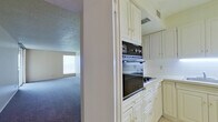 This single-floor, 2-bedroom, 1-bathroom unit offers a practical and well-organized layout designed to maximize its comfortable footprint. The living area features soft wall-to-wall carpeting, neutral-toned walls, and a textured ceiling, creating a warm and inviting atmosphere. A pass-through window connects the living space directly to the kitchen, enhancing the open feel between the two areas. Sliding glass doors lead out to a balcony, allowing natural light to fill the room and providing outdoor access with open views.

The kitchen is equipped with white cabinetry featuring gold-tone hardware, a built-in wall oven, a cooktop, and a stainless steel refrigerator. Light tile flooring runs through the kitchen and hallway areas, providing a clean contrast to the carpeted rooms.

The spacious primary bedroom is generously sized, featuring large sliding glass doors that open to the balcony, an additional window for cross-ventilation, and soft carpeting throughout. The second bedroom also offers carpeted flooring and a built-in closet with convenient shelving.

The bathroom includes a full tub-shower combination with white square tile surround, a vanity with a marble-style countertop, a mirrored medicine cabinet, and warm tile flooring. Hallways connect the rooms efficiently, completing the cohesive and functional floor plan.