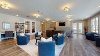 Located at 1733 Bellmeadow Dr in Lancaster, Ohio, this single-floor community clubhouse offers a thoughtfully designed gathering space built for both relaxation and socializing. The open-concept layout flows seamlessly across wood-look plank flooring throughout, creating a cohesive and inviting atmosphere.

The main lounge area serves as the centerpiece of the space, featuring a striking floor-to-ceiling tile-surround fireplace flanked by a wall-mounted flat-screen TV. Comfortable seating arrangements — including plush blue armchairs, patterned accent chairs, and a large sectional sofa — are thoughtfully arranged to encourage conversation and leisure. A reception or concierge-style desk anchors one end of the room, adding a welcoming, organized touch.

A sunlit seating nook lines one full wall with expansive multi-pane windows that overlook the outdoor swimming pool and surrounding grounds, filling the space with natural light and offering pleasant views year-round. French doors provide direct access to the pool area.

The fully equipped kitchen features white shaker-style cabinetry with glass-front upper cabinets, granite countertops, stainless steel appliances including a French door refrigerator, wall oven, and microwave, as well as a central island with bar seating and pendant lighting. A built-in desk area adds functional versatility to the space.

Together, these elements make this clubhouse a well-rounded, attractive amenity space.