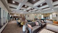 Located at 101 Hollow Tree Ln in Houston, TX, this single-floor community clubhouse is designed to serve as a dynamic social and functional hub. The centerpiece of the space is a generously sized open-concept great room featuring a striking coffered ceiling with dark wood inlays and recessed lighting that adds architectural depth and warmth. This area seamlessly connects a comfortable lounge with leather sofas, a game room with a full-size pool table, and a stone fireplace that anchors the space with a classic touch. Multiple dining tables with colorful modern chairs provide ample seating throughout, while large windows and French doors invite abundant natural light and outdoor views. The full community kitchen is well-appointed with white cabinetry, granite countertops, a wood-plank backsplash, stainless steel appliances, a central island with bar seating, and a built-in wine rack. A dedicated lounge nook features vibrant teal accent walls, a wall-mounted TV, and a sliding barn door, creating a cozy media retreat. Additional areas include a bright waiting or coffee nook with orange leather chairs and garden views, a small private office or media room with a wall-mounted TV and workstation, and a welcoming entryway with colorful accent seating and local Houston-themed artwork throughout.