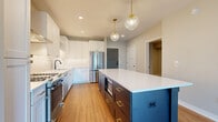 This single-floor unit is defined by a thoughtful blend of modern design and functional layout. The kitchen serves as a standout centerpiece, featuring a striking two-tone design with crisp white shaker cabinetry paired with a bold navy blue island topped by a clean white quartz countertop. Gold hardware accents and globe pendant lights with brass fittings add a refined, contemporary touch. Stainless steel appliances, including a French door refrigerator and gas range with a stainless hood, complete the space, while white subway tile backsplash and warm hardwood flooring tie the aesthetic together cohesively.

The open living area extends from the kitchen, continuing the hardwood flooring and offering access to an outdoor balcony through large sliding glass doors, bringing in generous natural light. Neutral-toned walls throughout create a calm, versatile backdrop.

Bedrooms feature plush carpet flooring and large windows with views of surrounding greenery, while a dedicated hallway connects to a walk-in closet and a well-appointed bathroom. The bathroom is highlighted by a frameless glass shower enclosure with large-format marble-look tile walls and matte black fixtures, adding a luxurious finishing detail to the overall space.