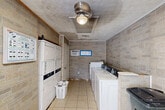 This shared laundry facility at 901 Crooked Creek Drive in Lufkin, Texas, offers a practical and functional space designed to meet everyday laundry needs. The room is finished with stone-look textured wall panels in warm beige and gray tones, lending a durable and easy-to-maintain interior aesthetic. Light-colored ceramic tile flooring runs throughout, providing a clean, hard-wearing surface well-suited for the demands of a high-traffic utility space.

The laundry room is equipped with multiple top-load washing machines lined along one wall, offering ample capacity for simultaneous loads. On the opposite side, a set of stacked dryer units maximizes the use of vertical space, efficiently accommodating the room's compact footprint. A wall-mounted air conditioning unit ensures the space remains comfortable year-round.

Overhead, a ceiling-mounted light fixture provides consistent illumination throughout the room. A textured ceiling adds a subtle decorative element to the otherwise utilitarian space. The room is accessed through a standard entry door, with a window allowing a degree of natural light. Posted informational signage and a fire extinguisher reflect attention to safety and user guidance. A utility trash receptacle is also present, supporting general cleanliness. Overall, this laundry facility is a straightforward, well-equipped space designed for convenience and practicality.