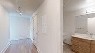 Located in Washington, DC's vibrant 20036 corridor, this modern 2-bedroom, 2-bathroom residence offers a thoughtfully designed single-level layout with a clean, contemporary aesthetic throughout. Light-toned hardwood flooring flows seamlessly across all main living areas, complementing the crisp white walls and abundant natural light.

The open-concept living and kitchen area serves as the heart of the home, anchored by expansive floor-to-ceiling windows that frame impressive cityscape views and allow sunlight to fill the space. The kitchen features stainless steel appliances and white cabinetry, creating a sleek, functional environment. Architectural columns add a refined structural detail to the living area, which also provides access to an outdoor space.

Both bedrooms are well-proportioned, each offering large windows with urban views and ample closet storage. The primary bedroom includes a walk-in closet with wire shelving systems for organized storage. The two bathrooms are finished with striking marble-style tile — one featuring a glass-enclosed walk-in shower, the other a full soaking tub and shower combination — both with warm wood-toned vanities and light tile flooring. A connecting hallway and dedicated closet complete this efficiently designed, light-filled urban residence.