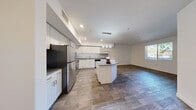 Located at 9110 W Tropicana in Las Vegas, Nevada, this well-designed one-bedroom, one-bathroom residence offers a thoughtful layout across a single floor. The open-concept living area seamlessly connects the kitchen, dining, and living spaces, creating a bright and functional environment. The kitchen is a standout feature, showcasing white shaker-style cabinetry, gray subway tile backsplash, dark countertops, a center island with pendant lighting overhead, and a full suite of stainless steel appliances including a refrigerator, gas range, and microwave. Wood-look plank flooring runs throughout the main living areas, adding warmth and a cohesive aesthetic. The spacious bedroom is finished with plush carpeting, a ceiling fan, and direct access to the balcony through a glass door, allowing for natural light and outdoor ventilation. The bathroom is cleanly appointed with white tile and vanity cabinetry. Additional conveniences include a dedicated laundry area, a private balcony, and a generous closet for storage. Recessed lighting and large windows contribute to a bright and airy ambiance throughout the unit.