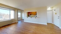 Located at 5323 Connecticut Ave NW in the Chevy Chase neighborhood of Washington, DC, this single-floor residence offers a clean, functional layout with thoughtful design details throughout. The open living area is anchored by warm hardwood flooring and neutral wall tones, creating a bright and welcoming atmosphere. Multiple windows allow generous natural light to fill the space, with views of the surrounding neighborhood streetscape. A pass-through window with a granite countertop bar connects the living area to the kitchen, promoting an open, communicative flow between the two spaces. The kitchen is efficiently arranged with warm wood cabinetry, granite countertops, a stainless steel sink, and black appliances including a gas range, microwave, and refrigerator, all set on light tile flooring. The bedroom is a well-proportioned room with the same hardwood flooring as the living area, featuring a large picture window that frames an outdoor view and draws in abundant sunlight. The bathroom is finished with classic white subway tile wainscoting, tile flooring, a single vanity, and a full bathtub with shower. The overall aesthetic is clean and understated, with consistent neutral tones and practical finishes throughout.