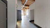 Located at 300 S Firestone St in Gastonia, NC, this industrial-style loft blends historic character with modern finishes across a single open floor plan. The space is defined by striking exposed brick walls, soaring ceilings with original wood beam construction, and polished concrete floors throughout, creating a bold and airy atmosphere.

Oversized multi-pane factory windows flood the main living area with abundant natural light, highlighting the architectural details at every turn. A standout red barn door adds a dramatic focal point against the raw brick backdrop, while exposed ductwork and ceiling fans reinforce the industrial aesthetic.

The well-appointed kitchen features warm wood cabinetry, granite countertops, stainless steel appliances including a range, microwave, dishwasher, and refrigerator, along with a central island that provides additional workspace and seating. A farmhouse-style sink completes the functional layout.

Two bathrooms offer clean, modern finishes consistent with the rest of the space. One bathroom includes a full tub-shower combination, wood vanity with granite countertop, and a large mirror, while the second bathroom features a similar vanity and granite countertop. A hallway connects the private areas to the expansive main living space, ensuring a smooth and practical flow throughout.