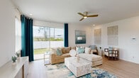 This two-story home offers a thoughtfully designed layout spread across two floors, delivering generous living space for residents and guests alike. The main floor hosts an open-plan living room, kitchen, and dining area that seamlessly connect for effortless everyday living and entertaining. The living room is bathed in natural light from large sliding glass doors that open to a private backyard, complemented by light hardwood-style flooring and a modern ceiling fan overhead. The kitchen is outfitted with crisp white shaker cabinetry, quartz countertops, stainless steel appliances, and a large island with sink — a highly functional and visually clean culinary space. The adjacent dining area features a bright window framed by teal curtains, carrying the home's coastal-inspired palette throughout. Upstairs, the primary bedroom is a serene retreat featuring a tray ceiling, dual windows with garden views, and light wood flooring. Its en-suite bathroom includes a glass-enclosed walk-in shower accented with blue subway tile and a white vanity with quartz countertops. A dedicated walk-in closet with wire shelving adds practical storage. Three additional bedrooms, each with natural light and outdoor views, are supported by three more full bathrooms. A dedicated laundry room with full-size washer and dryer completes the upper level.