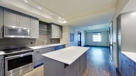 This well-designed two-bedroom, one-bathroom unit offers a thoughtful single-floor layout with modern finishes throughout. The open-concept kitchen anchors the living space and is outfitted with stainless steel appliances, including a refrigerator, range, microwave, and dishwasher. Gray shaker-style cabinetry pairs with white quartz countertops and a textured tile backsplash, while a substantial center island provides additional prep and seating space. Track lighting illuminates the kitchen, which flows seamlessly into the main living area featuring durable wood-look flooring.

The primary bedroom is a comfortable, well-proportioned room with wood-look flooring and a window offering natural light. The second bedroom features plush carpeting, a ceiling fan, and a window with exterior views. Both bedrooms include dark-trimmed accents that lend a contemporary touch.

The bathroom is finished with floor-to-ceiling white subway tile in the walk-in shower, which also features a built-in bench. A dark wood vanity with a white countertop and a large mirror complete the space.

A dedicated entry closet area features built-in coat hooks, a wooden bench, and an integrated desk, offering practical organization. Wood-look tile flooring runs through the main living and kitchen areas, tying the unit together with a cohesive, modern aesthetic.