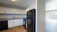 This single-floor unit offers a clean, modernized interior with consistent wood-look plank flooring running throughout every room, complemented by neutral gray walls and crisp white trim. The kitchen is thoughtfully equipped with white shaker-style cabinetry, granite-look countertops, a black gas range with overhead ventilation, a black refrigerator, and a stainless single-basin sink — providing both functionality and a cohesive aesthetic. The kitchen opens toward a dining or living area that features a sliding glass door with vertical blinds, allowing natural light to fill the space and offering direct outdoor views. The living areas are generously proportioned, providing flexible use of space. Multiple bedrooms are present, each featuring wood-look flooring, neutral walls, and windows with vertical blinds that allow natural light. One bedroom includes a built-in closet with a rod and open shelving. The full bathroom features a white vanity with a granite-look countertop, a tub-shower combination with tiled surround, and a small window for natural ventilation. Recessed lighting and flush-mount ceiling fixtures provide consistent illumination throughout. The overall ambiance is clean, fresh, and move-in ready.