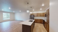 This single-floor residence is designed with an open-concept layout that seamlessly connects the living and kitchen areas. The living space is generously sized, featuring light wood-tone flooring, recessed lighting, and a large window that allows natural light to fill the room. A baseboard heating system runs along the perimeter walls throughout the unit.

The kitchen is well-appointed with warm-toned shaker-style cabinetry that extends to the upper walls, providing ample storage. Stainless steel appliances include a refrigerator, range with microwave above, and additional counter appliances. A center island with a dark base and white countertop houses a single-basin sink and is illuminated by two pendant lights, making it a functional focal point of the space.

The bedroom offers plush carpeting, a ceiling fan with light, and a window with blinds. A doorway leads directly into a walk-in closet with built-in shelving, providing organized storage solutions.

The bathroom includes a white vanity with a white countertop, an undermount sink, chrome fixtures, and a large mirror. A separate walk-in shower with a white acrylic surround and chrome hardware, along with wood-tone flooring, completes the space with a clean, functional aesthetic.