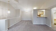 This two-floor home offers a thoughtfully laid-out interior with a blend of functional design and comfortable living spaces. The upper level is highlighted by dramatic vaulted ceilings that soar overhead, creating an airy, open atmosphere in the main living and dining areas. Plush wall-to-wall carpeting runs throughout, adding warmth underfoot, while neutral-toned walls provide a versatile backdrop. A elegant chandelier anchors the dining area, and a pass-through opening connects it seamlessly to the kitchen, enhancing the open-concept feel. A striking arched window at the upper level floods the space with natural light.

The kitchen is well-appointed with white cabinetry trimmed in warm wood accents, offering generous storage through both upper and lower cabinets. Light-toned countertops provide ample prep space, complemented by a stainless steel double-basin sink, an electric range, and a refrigerator. Light wood-look flooring ties the kitchen together with a clean, practical finish.

The bathroom features wood-look flooring, a single vanity with a large mirror, and a full tub-shower combination. The bedrooms are carpeted and bright, with easy access to closet space. A staircase connects the two floors, completing this well-organized, multi-level home.