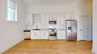 Located at 650 E Brooklyn Village Ave in Charlotte, NC, this single-floor unit offers a clean, modern aesthetic throughout. The open-concept layout is anchored by warm light wood flooring that flows seamlessly across all living areas, creating a cohesive and inviting atmosphere.

The kitchen is a standout feature, outfitted with white shaker-style cabinetry, open shelving, light quartz countertops, a white subway tile backsplash, and a full suite of stainless steel appliances including a range, over-the-range microwave, dishwasher, and a side-by-side refrigerator with an in-door ice and water dispenser. The crisp white walls and abundant upper cabinetry provide generous storage.

The main living area is bright and airy, benefiting from natural light that pours in through large French doors with transom windows above, offering views to the outdoors. Recessed lighting complements the natural illumination throughout the space.

An additional room features a clerestory-style window positioned high on the wall, keeping the space bright while maintaining privacy — well-suited as a bedroom or flexible-use room.

The bathroom is neatly appointed with a white vanity, taupe quartz countertop, a framed mirror, and stylish bar lighting above, all continuing the home's consistent modern design palette. The overall ambiance is light, neutral, and move-in ready.